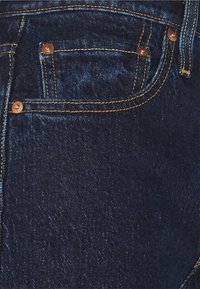 Mörkblå denimjeans med fem fickor, kopparnitar och guldfärgade sömmar, med en slät yta och en lätt lyster.