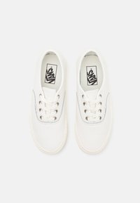 Baskets en toile blanche avec des accents argentés, présentant un bout rond, une fermeture à lacets plats et un logo sur la semelle intérieure. Texture lisse et design minimaliste.