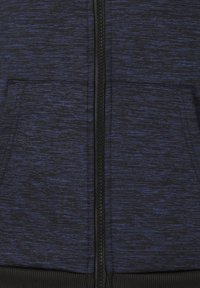 Sweat à capuche zippé bleu marine avec un tissu texturé comportant des flecks gris foncé, poches kangourou à l'avant et une fermeture éclair noire avec un tirant texturé.