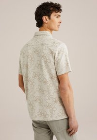 Camisa de manga corta en tejido beige claro con patrones florales marrones, con cuello tipo spread y un corte relajado, vista desde la espalda.