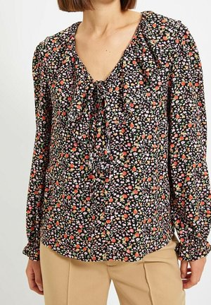 Blouse noire à fleurs avec un col en V et un détail à nouer, présentant des fleurs colorées et des poignets élastiques. Le motif comprend des accents roses et oranges.