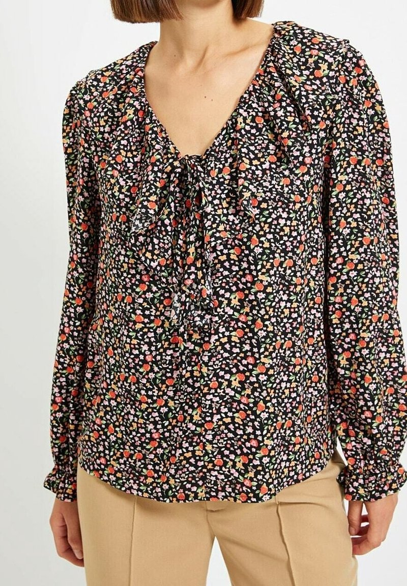 Blusa nera floreale con scollo a V e dettaglio a fiocco, caratterizzata da fiori colorati e polsini elasticizzati. Il motivo include accenti rosa e arancioni.