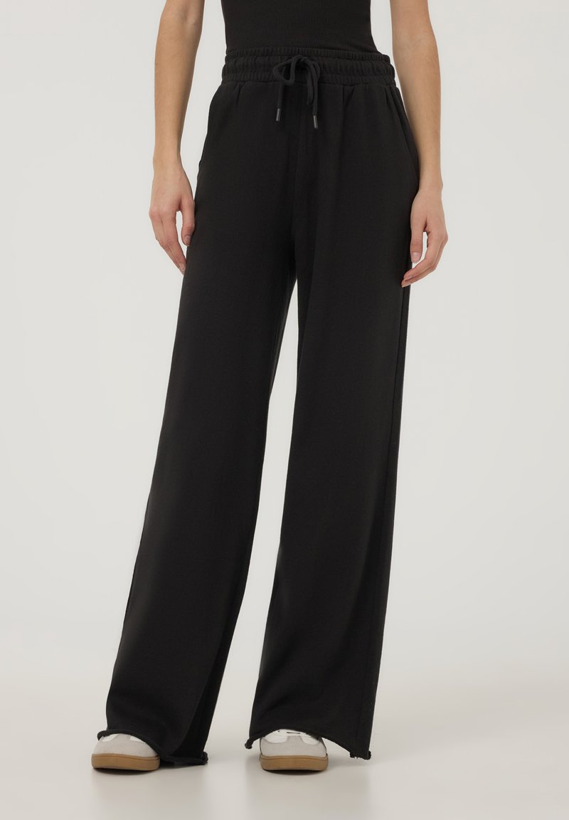 Pantaloni neri a gamba larga realizzati in tessuto morbido, dotati di una vita elastica regolabile con cordoncino e tasche laterali.