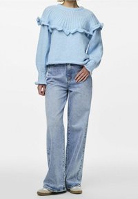 Pull en tricot bleu clair avec col côtelé et ourlet volanté, associé à un jean flare en denim clair taille haute et des chaussures beiges.