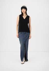 Svart ermeløs topp med V-hals, kombinert med et langt denimskjørt med slag foran. Modellen har på seg en svart-hvit stripete lue og lyse sko.