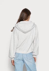 Felpa corta grigia chiara in tessuto morbido con un ampio cappuccio, polsini e orlo a coste. Abbinata a jeans in denim azzurro chiaro dal taglio rilassato.