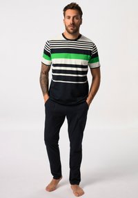 Pruhovaná košile s krátkým rukávem v námořnické, bílé a zelené barvě. V kombinaci s námořnickými kalhotami, obě z lehkého materiálu. Model stojí bosý s rukama v kapsách.