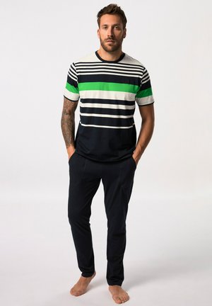 Camisa de manga corta a rayas en azul marino, blanco y verde. Combinada con pantalones azul marino, ambos de tejido ligero. El modelo está de pie descalzo con las manos en los bolsillos.