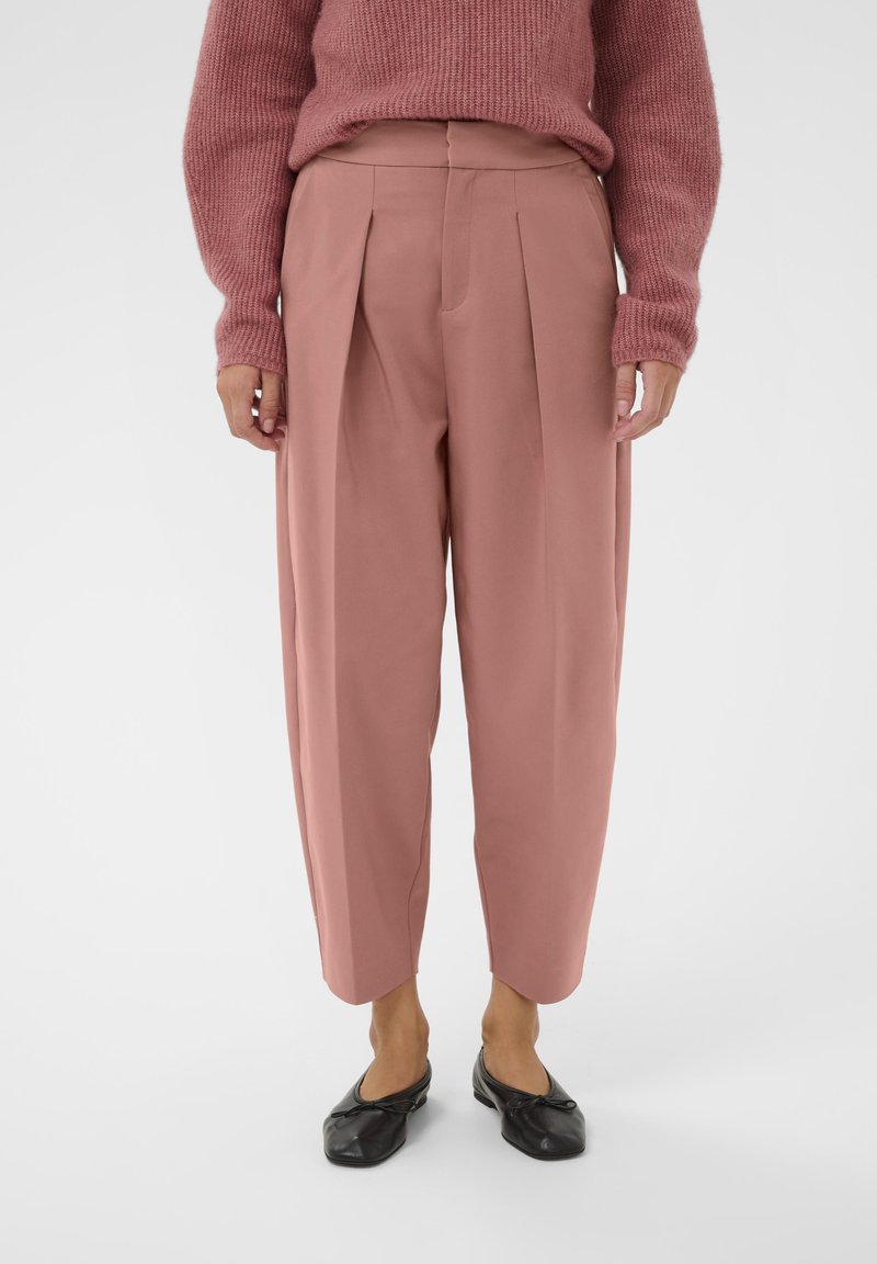 Pantaloni roz, cu talie înaltă, cu pliuri, formă conică și textură moale. Asortați cu pantofi negri, comozi, cu un design simplu.