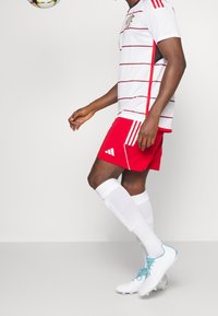 Red and white striped athletic shirt, red shorts, white knee-high socks, and white cleats with blue accents. Soccer ball in mid-air.