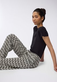 Top corto nero a maniche corte abbinato a pantaloni larghi e fantasia con motivo a foglie nere su sfondo crema.