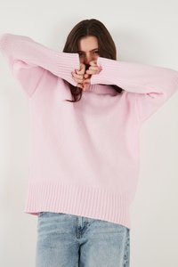 Heller rosa gestrickter Pullover mit geripptem Saum und Bündchen, lockere Passform. Modell teilweise verdeckt, trägt hellblaue Jeans.