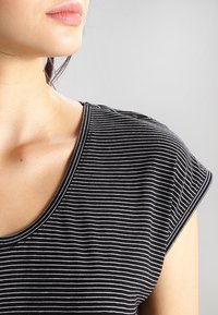 Svart- och vitrandig t-shirt med djup halsringning och korta ärmar, tillverkad av ett mjukt tyg som visar en jämn textur och avslappnad design.