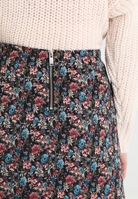 Blommig kjol med en mörk bakgrund och blåa och rosa blommor, midjezipper och textil med varierande blommönster.