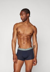 Marineblå boxershorts med en grå elastisk midje som har "TOMMY HILFIGER"-merking. Glatt, tettsittende design uten synlige mønstre.