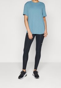 Blå kortärmad t-shirt matchad med svarta leggings och svarta sneakers. T-shirten är löst sittande, medan leggingsen sitter åtsittande.