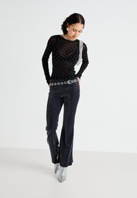 Schwarze, durchsichtige Langarmbluse mit weißen Punkten, kombiniert mit glitzernden schwarzen Schlaghosen und silbernen, spitzen Ankle Boots. Abgerundet mit einem Gürtel.