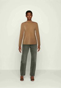 Top ajustado de mangas longas, bege, com decote redondo, combinado com jeans de corte reto, cinza escuro. Modelo usa sandálias pretas de salto alto.