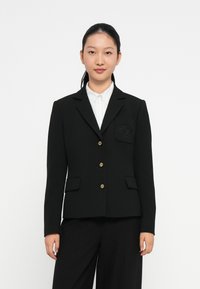 Blazer noir avec des boutons dorés, revers en pointe et poches avant doubles. Comprend une poche sur la poitrine à gauche avec un détail texturé.