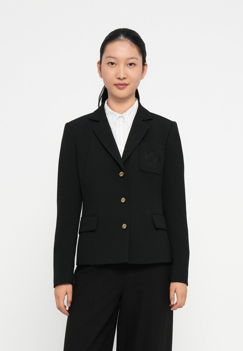 Blazer noir avec des boutons dorés, revers en pointe et poches avant doubles. Comprend une poche sur la poitrine à gauche avec un détail texturé.