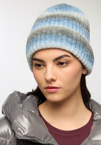 Wełniana czapka beanie z paskowanym wzorem w jasnoniebieskich, ciemnoniebieskich i szarych odcieniach. Żebrowana tekstura z zaokrąglonym czubkiem i ciepłym designem.