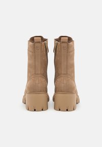 Botas de tobillo de cuero marrón claro con suela de goma gruesa, cremalleras laterales dobles y superficie texturizada. Puntera redondeada y diseño de talón reforzado.