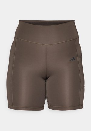 Brune idrettsshorts med en jevn tekstur, høy midje og kontrasterende mørke sømmer. Har en liten svart logo på venstre side.
