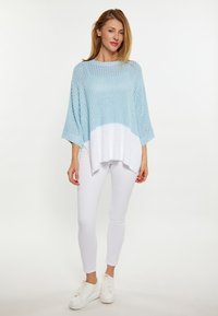 Pullover lavorato a maglia di colore azzurro chiaro con orlo bianco, caratterizzato da un design ampio e oversize. Abbinato a pantaloni aderenti bianchi e sneakers bianche.