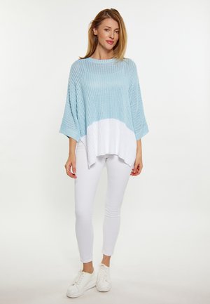Pullover lavorato a maglia di colore azzurro chiaro con orlo bianco, caratterizzato da un design ampio e oversize. Abbinato a pantaloni aderenti bianchi e sneakers bianche.