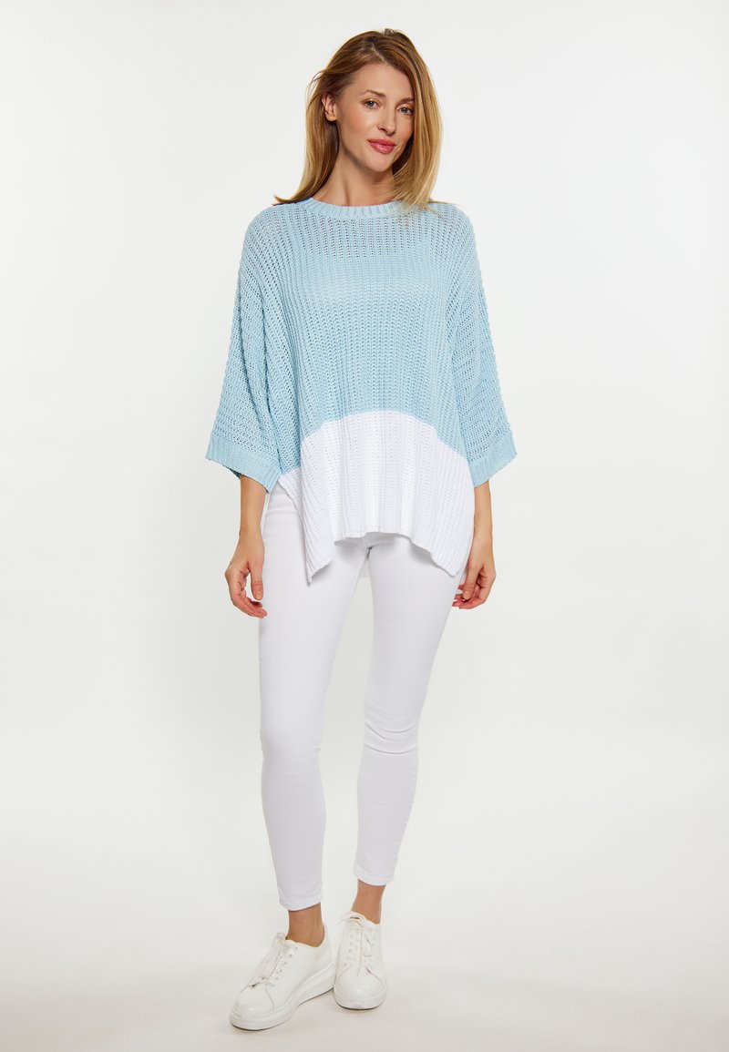 Pullover lavorato a maglia di colore azzurro chiaro con orlo bianco, caratterizzato da un design ampio e oversize. Abbinato a pantaloni aderenti bianchi e sneakers bianche.