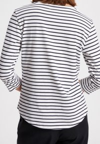 Maglietta bianca in cotone a maniche lunghe con righe orizzontali blu navy, orlo curvo e vestibilità morbida. Presenta un collo a giro e maniche lunghe fino ai polsi.