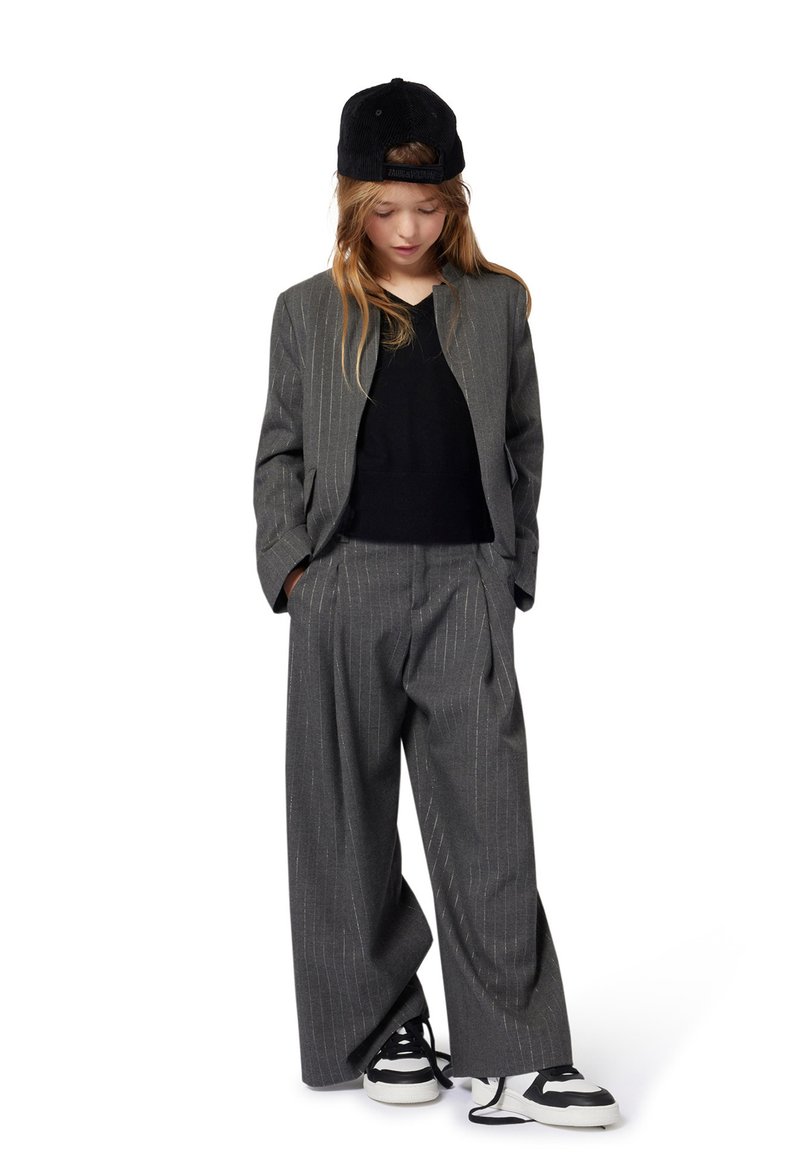 Grijs gestreept pak met losse broek en een bijpassende blazer, gecombineerd met een zwart T-shirt en een zwarte baseballcap; witte en zwarte sneakers.