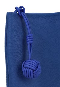 Niebieska skórzana torba o fakturowanej powierzchni, zawiązywana na niebieski sznurek z supełkiem. Gładkie wykończenie z zaokrąglonym detalem supełka.