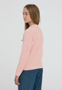 Różowy sweter na drutach z teksturowanym wzorem, z długimi rękawami i okrągłym dekoltem, w połączeniu z niebieskimi dżinsami.