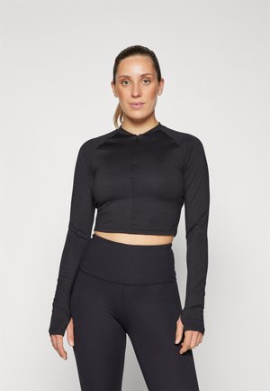 Zwarte cropped lange mouw top van gladde, rekbare stof met een hoge halslijn en ritssluiting. Gepaard met hoge zwarte leggings.