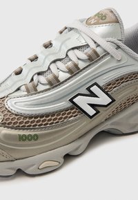 New Balance tenisice sa gornjim dijelom od srebrne mrežice, bež detaljima, crnim logotipom i teksturiranom potplatom s vidljivim detaljem "1000".