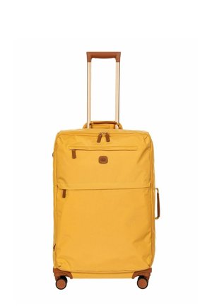 Valise jaune à roulettes avec poignée télescopique, poches zippées à l'avant, poignée latérale et quatre roues pivotantes sur fond blanc.