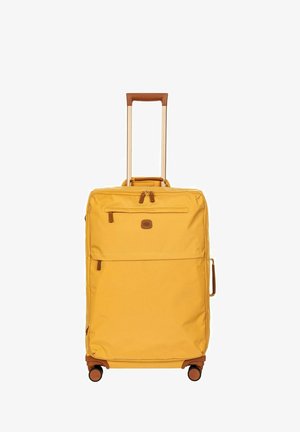 Valise jaune à roulettes avec poignée télescopique, poches zippées à l'avant, poignée latérale et quatre roues pivotantes sur fond blanc.