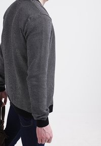 Svart och vit mönstrad tröja med rund hals, ribbade ärmar och nederkant. Materialet verkar mjukt med en strukturerad, prickig design.