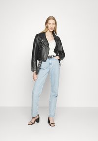 Zwarte leren bikerjack, witte top met kantafwerking, lichtblauwe hoogwaist jeans en zwarte blokhak sandalen.
