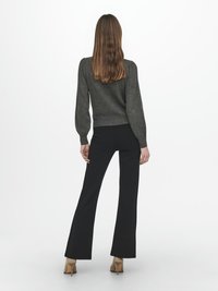 Grå stickad tröja med puffärmar, i kombination med svarta utsvängda byxor och beige klackskor, sedd bakifrån mot en vit bakgrund.