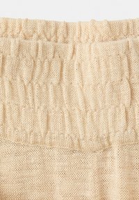 Tissu en tricot beige avec une texture côtelée en haut et un motif en tricot lisse en dessous, montrant la zone de la ceinture d'un vêtement.