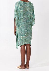 Zelený kaftan s paisley vzorem a splývavými rukávy, vyrobený z lehké látky. Rozparky na bocích zvyšují prodyšnost a usnadňují pohyb.