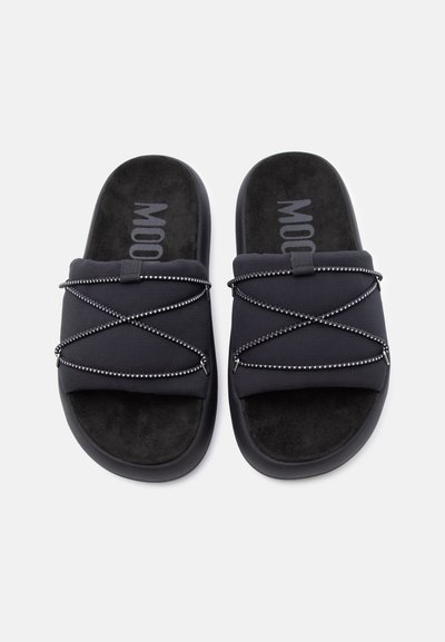 Ζευγάρι μαύρες παντόφλες slip-on με μαλακές σόλες και ελαστικά κορδόνια που διασταυρώνονται σε υφασμάτινους ιμάντες.