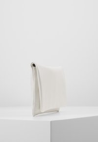 Minimalistyczna biała skórzana kopertówka stoi na białym podium na tle jasnoszarego, gładkiego tła.