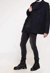 Svart ull peacoat med dubbelknäppning, bärs över en mörk tröja och svarta skinny jeans, kombineras med svarta snörkängor.
