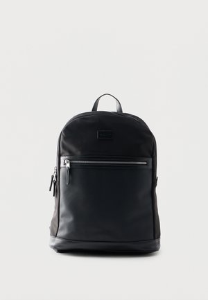 Zwart rugzak met voorvak met rits en een bovenste draaggreep, rechtopstaand tegen een effen lichte achtergrond.