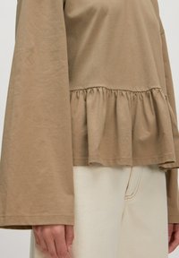 Braunes Langarmoberteil mit einem Peplum-Saum, aus weichem Stoff mit lockerem Schnitt, mit ausgestellten Ärmeln und glatter Textur.
