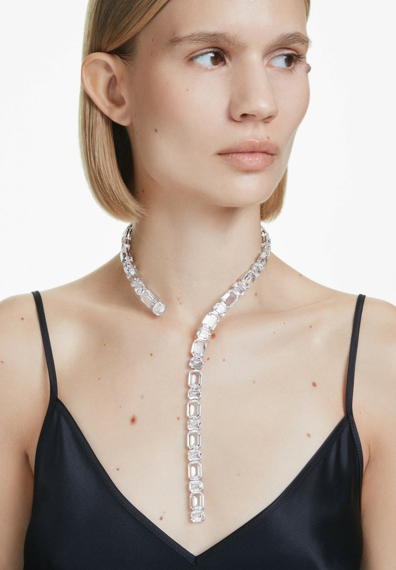 Collana di cristallo trasparente con maglie rettangolari, caratterizzata da una finitura liscia. Indossata su un indumento di satin nero, che ne esalta il design.