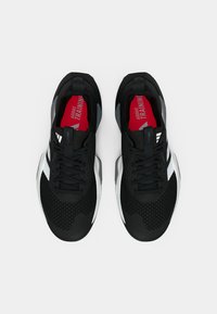 Ζευγάρι μαύρα και λευκά αθλητικά παπούτσια Adidas με επάνω μέρος από δίχτυ και κόκκινες εσωτερικές σόλες, εμφανιζόμενα από πάνω σε λευκό φόντο.